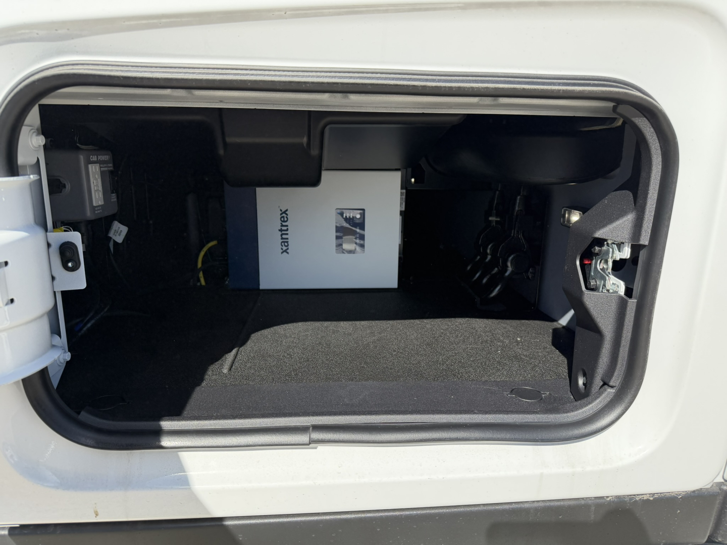 Truck cargo bay opening showing Xantrex inverter/box unit inside storage area with black carpeting and surrounding panels.