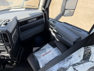 Cockpit of a Mack PR64T76H truck showing dashboard panels, steering column, and passenger seat with papers and manuals on it.