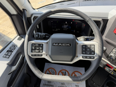 Mack PR64T76H truck cockpit with steering wheel and control panels showing Mack logo on center, digital display and various control buttons.