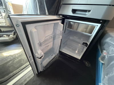 Truck interior showing a compact refrigerator/freezer unit with open doors in a cab area; freezer shelf and door compartments visible.