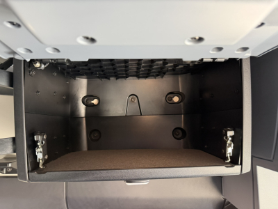 CABinet under dash area of a Mack PR64T76H truck showing open storage drawer with metal hinges and interior paneling