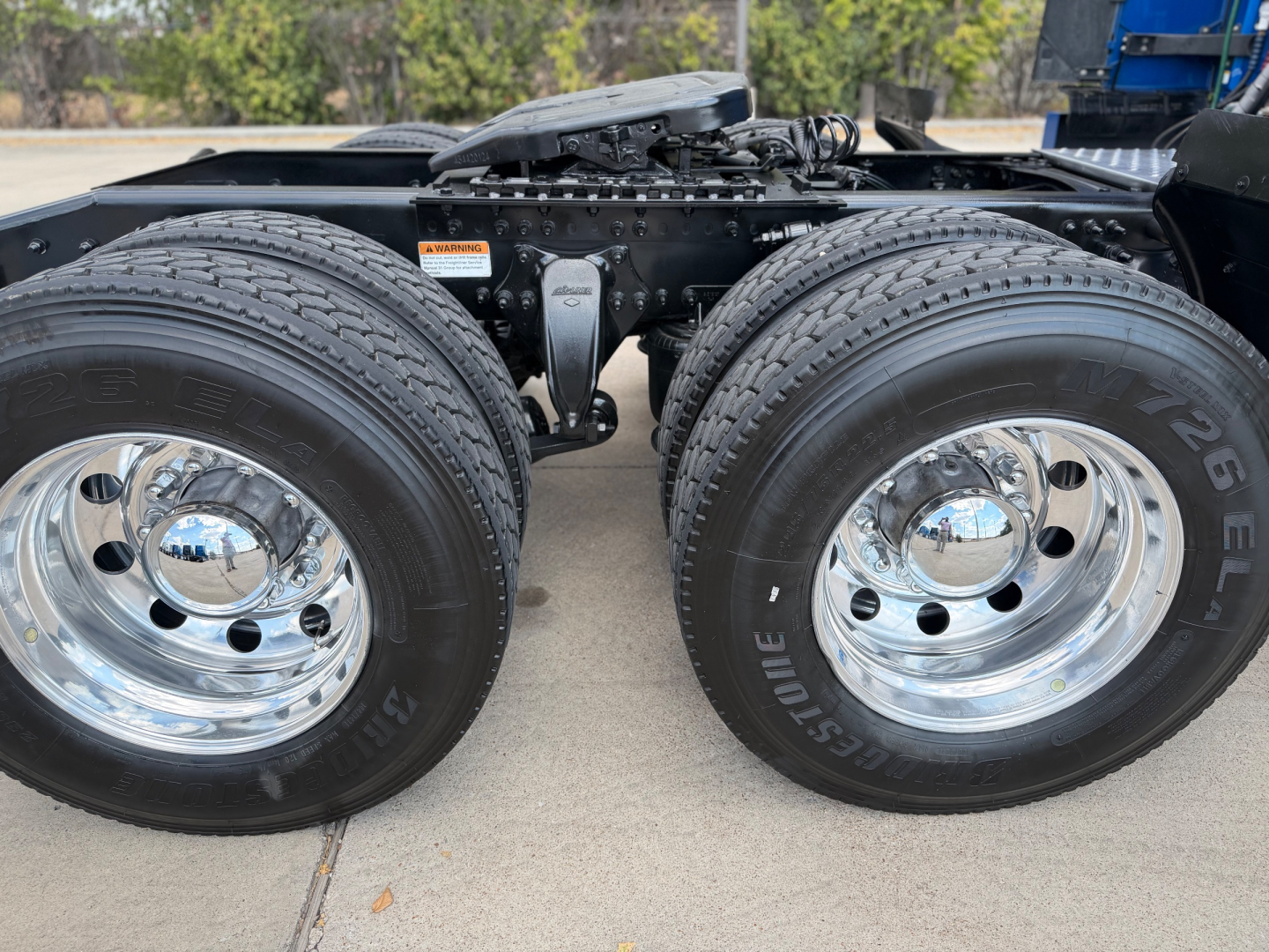 Dual rear axles with large tires and chrome wheels on Freightliner truck chassis; visible is the suspension U-bolt, air lines, and hitch area.