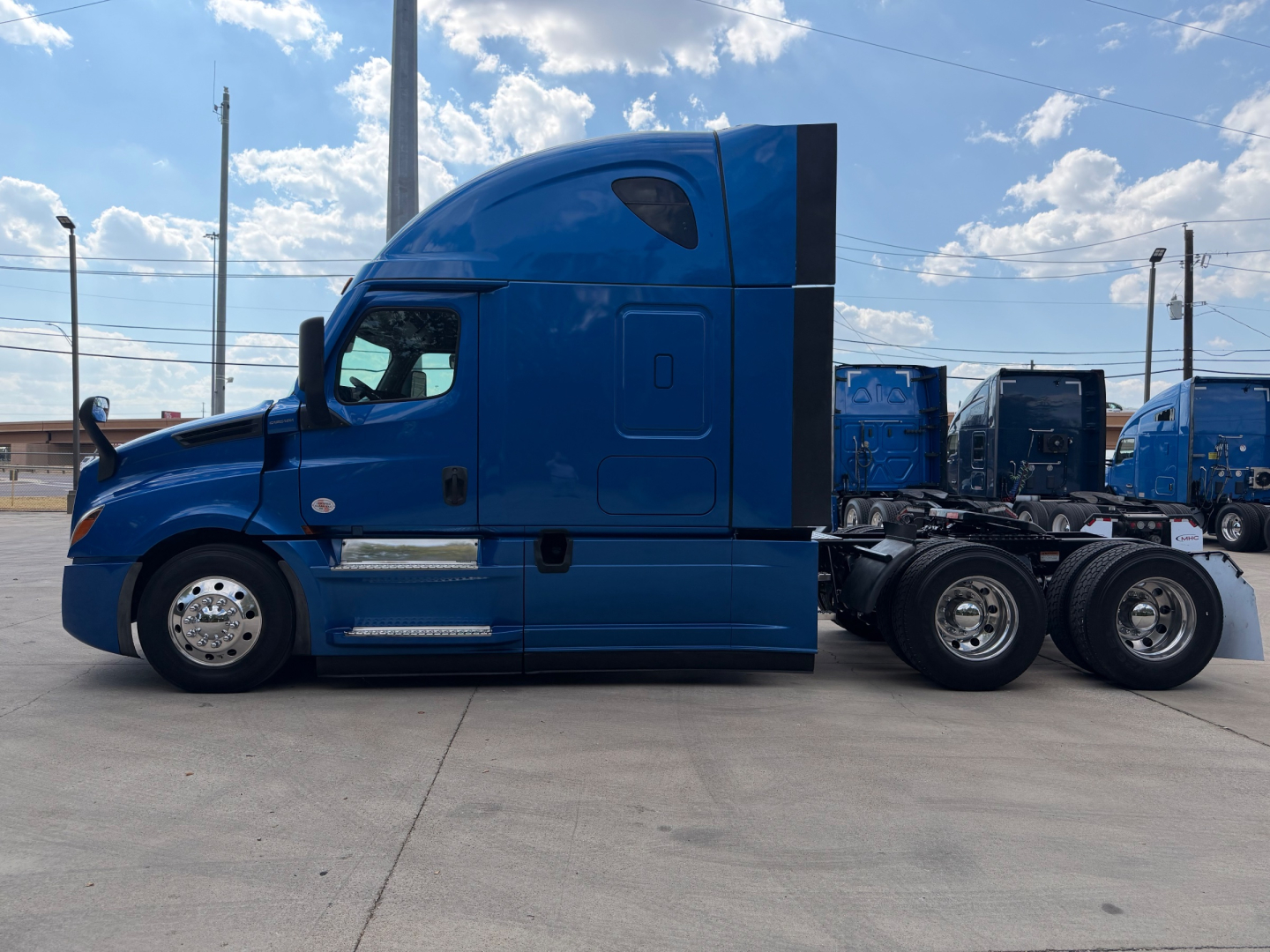 Blue Freightliner PT126064ST sleeper cab tractor, side profile view, shows diesel fuel tanks, chrome wheels, and tag axle configuration.