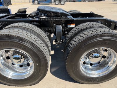Double rear axle of a Freightliner truck showing dual tires and chrome wheel hubs; frame and suspension components visible between the axles.