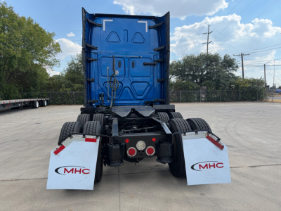 Rear view of a Freightliner tractor cab showing dual rear mud flaps with MHC logos, blue cab back, fifth wheel and drivetrain.
