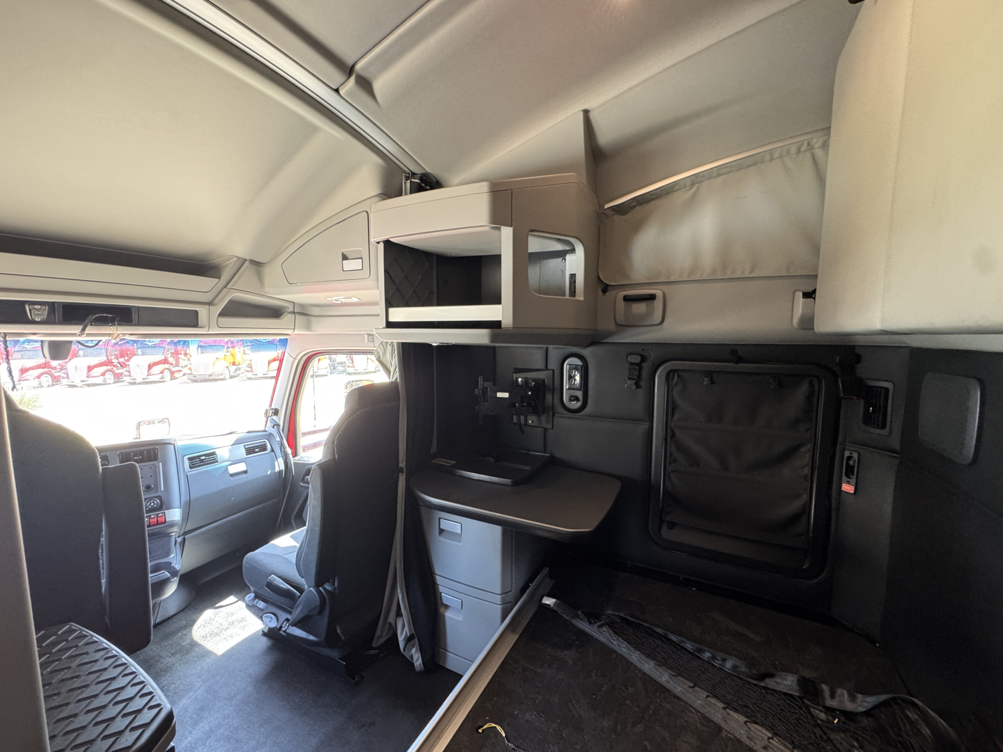Kenworth T680 cab interior showing sleeper area with overhead storage, desk/drawer, and side panel; dashboard and driver seat visible in foreground.