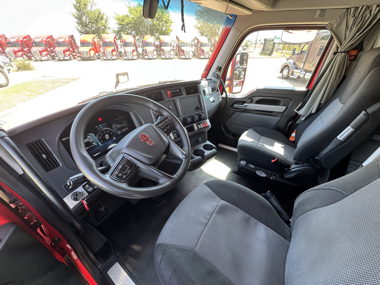 Kenworth T680 cab interior showing steering wheel, dashboard, driver seat, and passenger seat with center console.