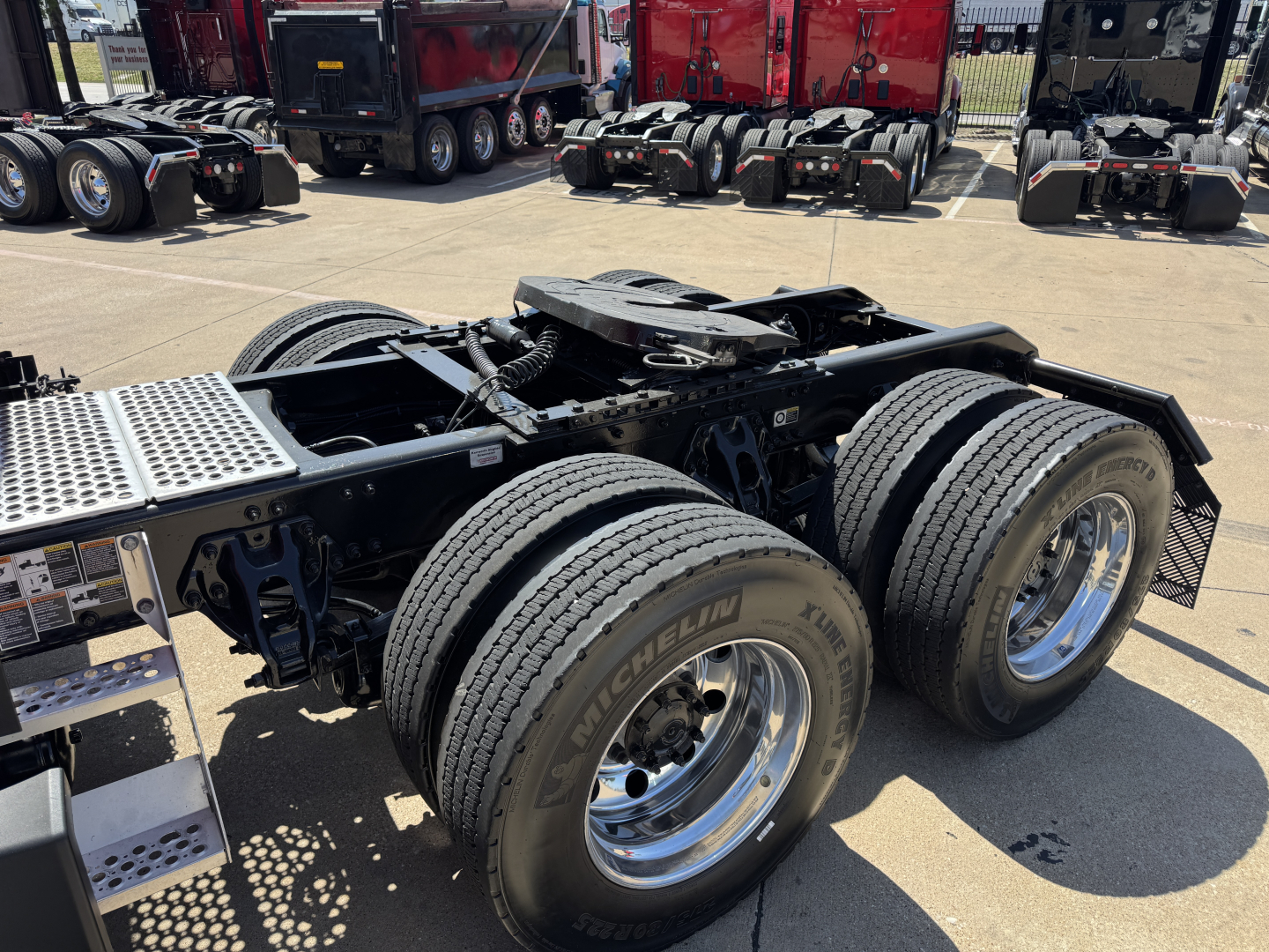 Kenworth T680 chassis with dual rear axles and large Michelin tires, visible fifth wheel and suspension components in a truck lot