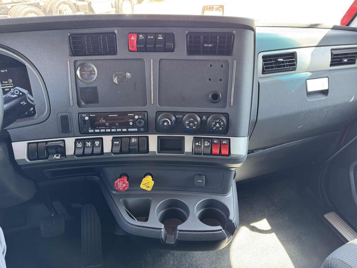 Kenworth T680 dashboard and center console view showing gauges, switches, climate controls, cup holders, and storage compartments.