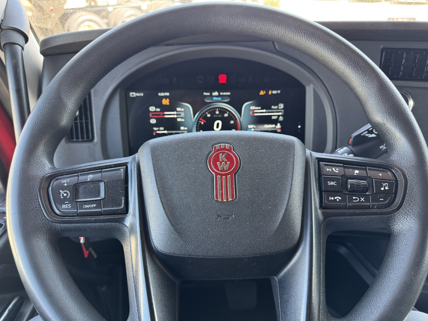 Kenworth truck interior steering wheel and dashboard view from driver seat showing Kenworth emblem, digital gauge cluster, and steering wheel controls.