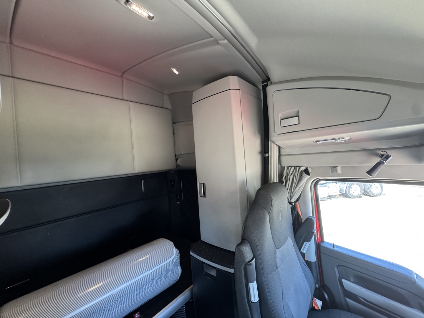 Kenworth truck interior 2023 T680 sleeper cab showing storage cabinet, bunk area, and driver seat with overhead console.