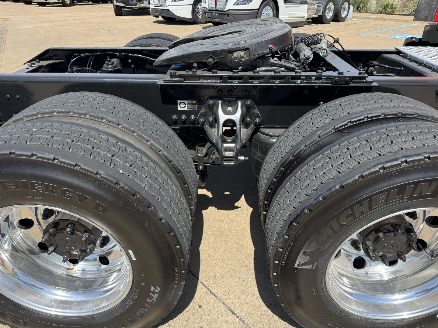 Kenworth T680 rear axle area showing dual rear wheels, chrome rims, and fifth wheel mount; visible fuel lines and chassis components in the center.