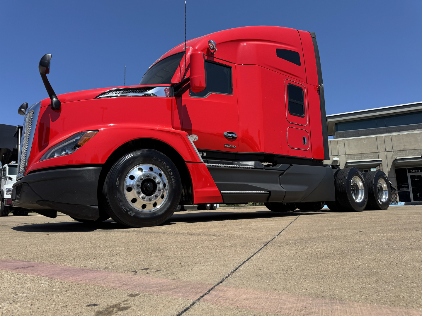 Kenworth T680 sleeper cab in red, side view showing front wheel, lower steps, and dual rear axles.