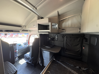 Kenworth T680 cab interior showing sleeper area with overhead storage, desk/drawer, and side panel; dashboard and driver seat visible in foreground.