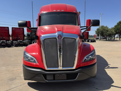 Kenworth T680 front view with red cab, chrome grille, black lower bumper, daytime highway setting.