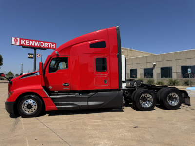Kenworth T680 tractor in red color, side profile view, showing sleeper cab and rear axles, at Kenworth dealership