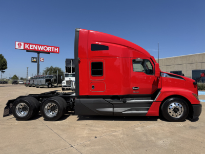 Kenworth T680 side view without trailer showing red cab and black chassis with Kenworth dealership sign in background.