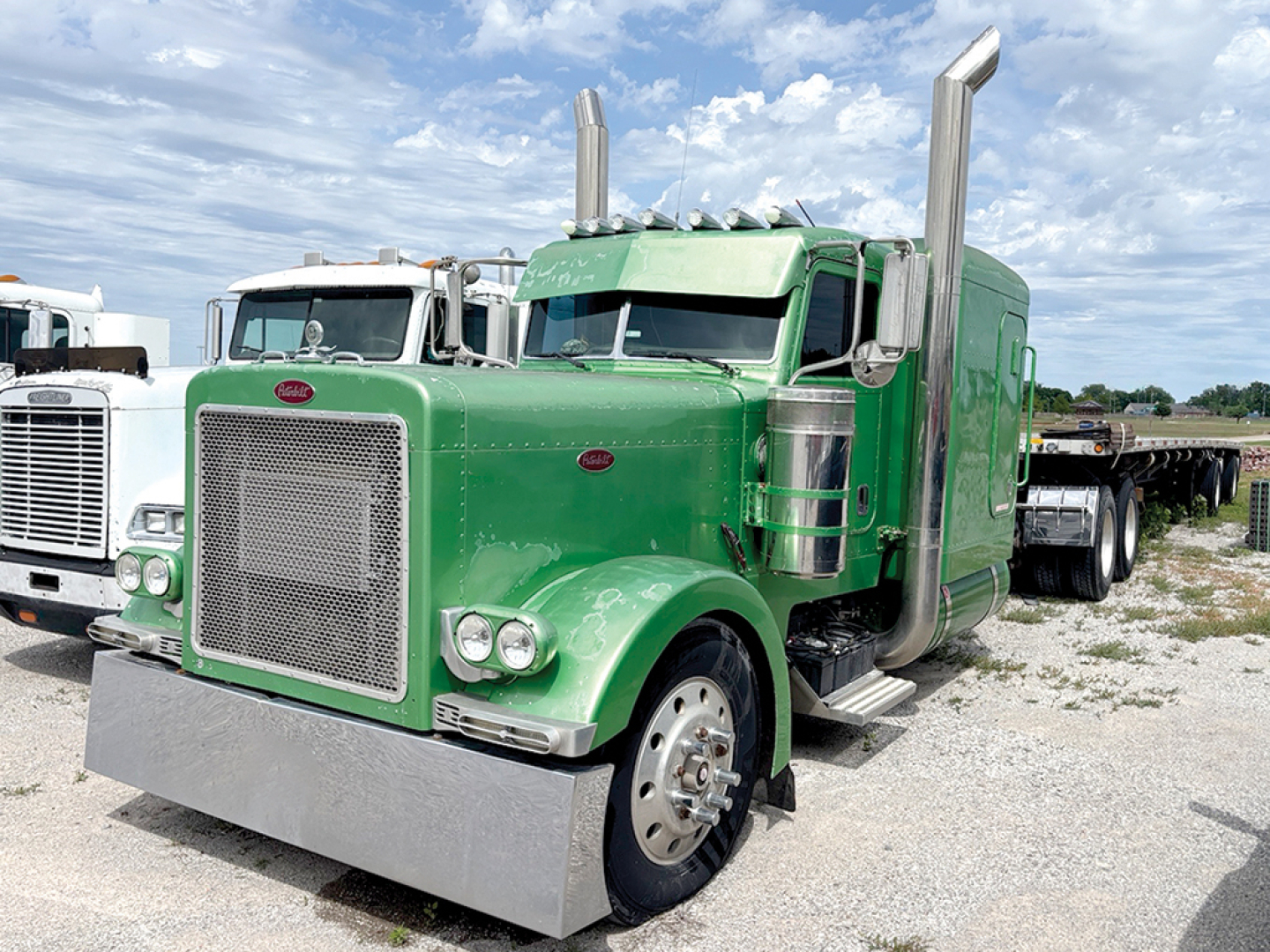 Peterbilt 379 extended hood truck in green in-service, front grille and large chrome exhaust stacks visible, with a wide front bumper.