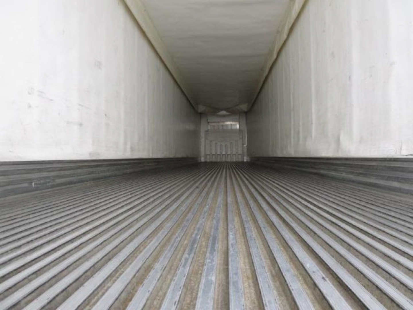Trailer interior showing ribbed floor of a refrigerated trailer with loading door at far end.