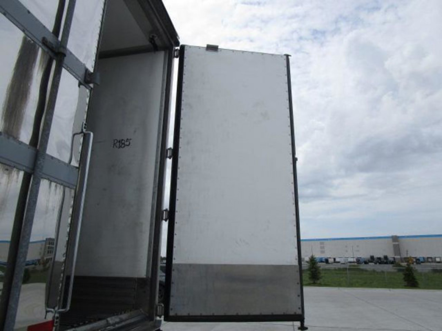 Trailer side door open showing interior of refrigerated utility trailer with metal panels and ramp, exterior gray/white surfaces visible.