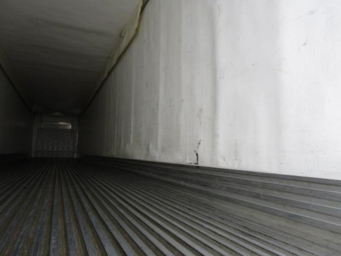Trailer interior showing corrugated floor and white interior walls, empty cargo space with light at far end.