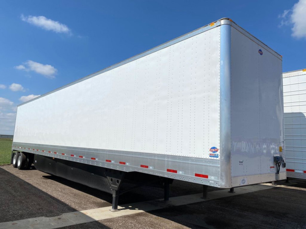 Trailer side view showing a white enclosed utility trailer with dual axles and reflective red/white stripes along the bottom edge.
