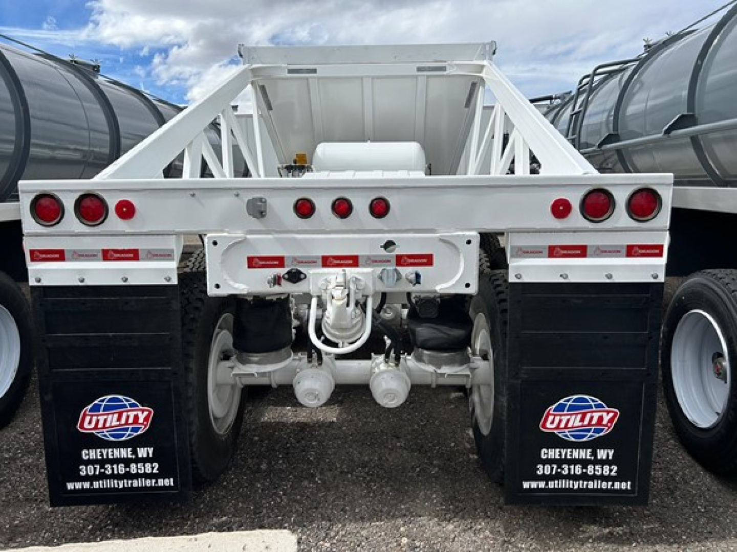 Dump trailer rear view showing tandem axles, suspension, and hydraulic line connections on Versa trailer with Utility mud flaps and red rear lights.