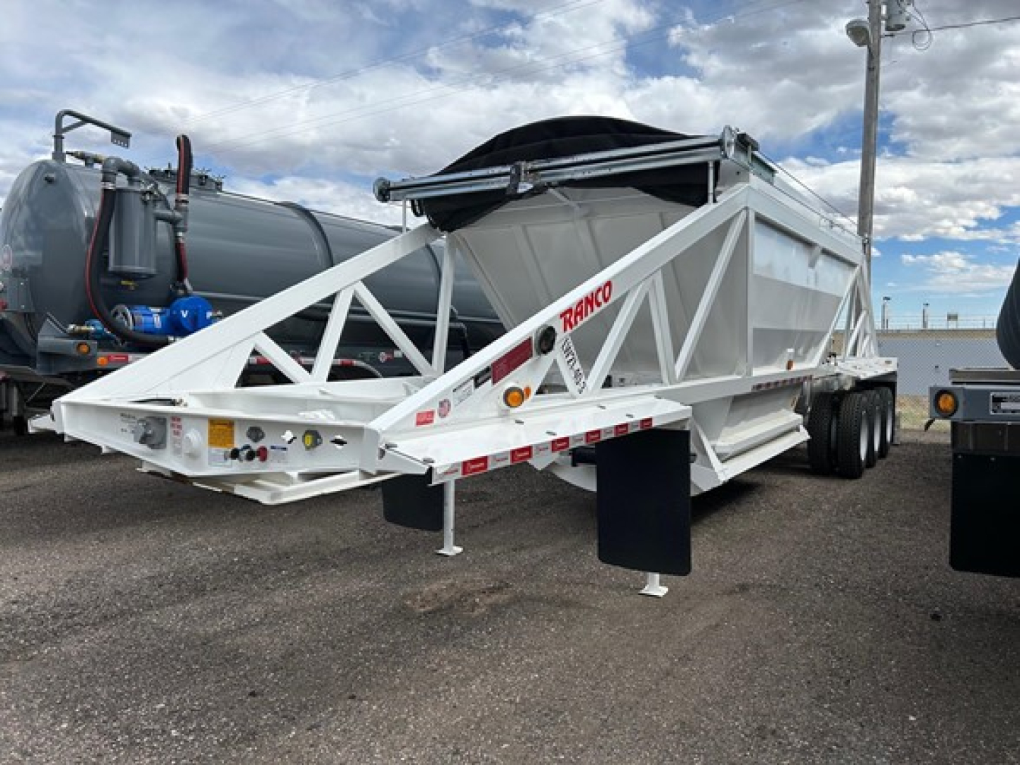Ranco Versa dump trailer in an outdoor lot showing white structural frame and dual-axle configuration with RANGO branding and reflective markings.
