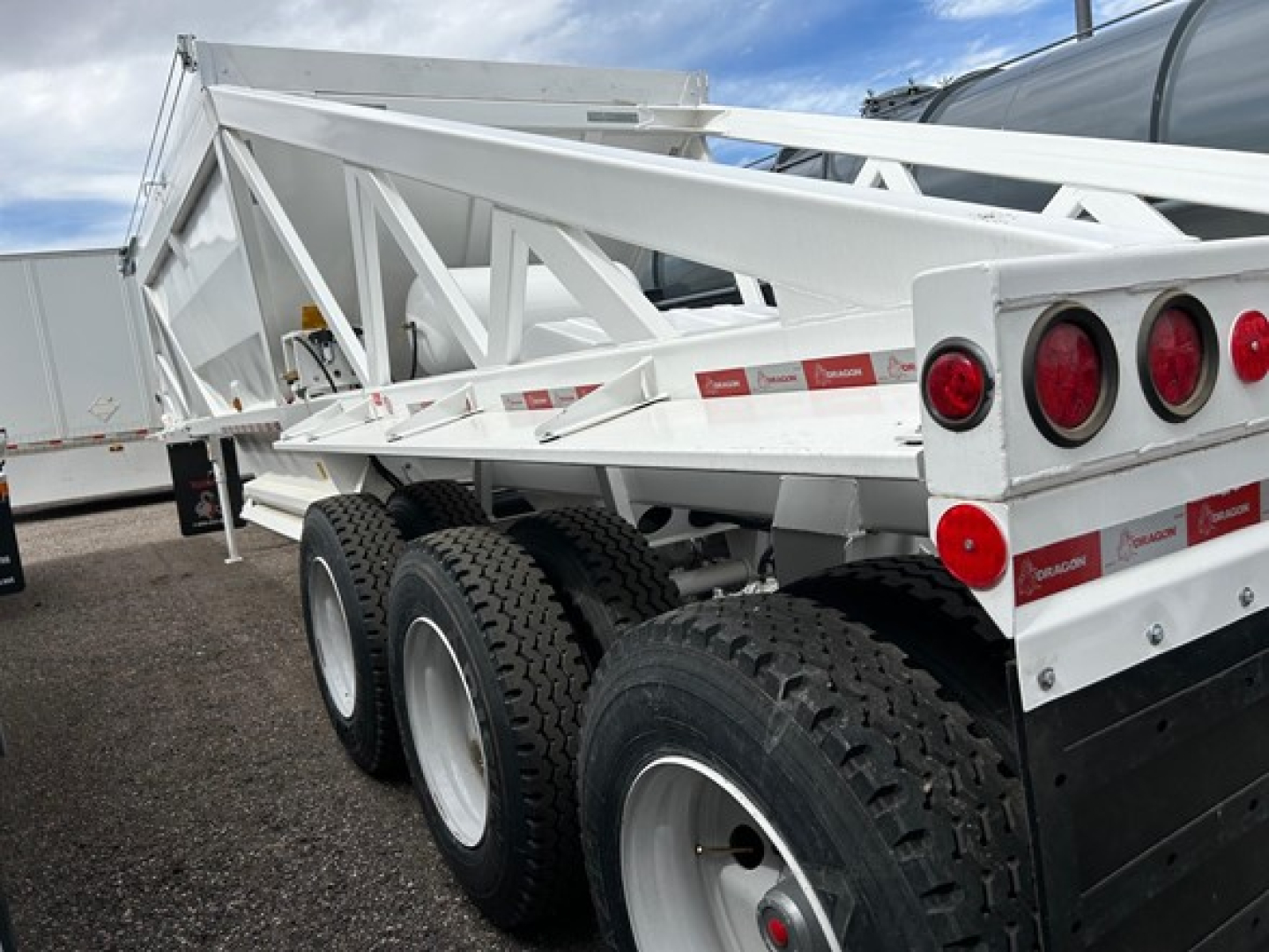 Dump trailer with white frame and triple-axle configuration, showing rear lights and structural sides.