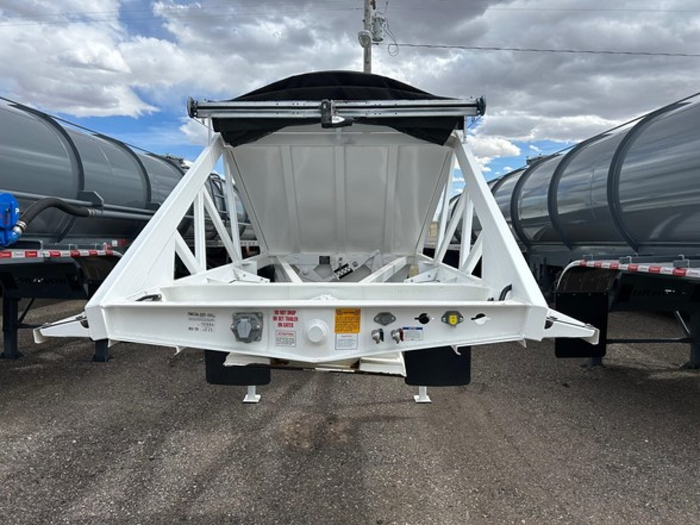 Dump trailer hopper with white frame and black tarp, rear view showing spread axles and control panel labels.