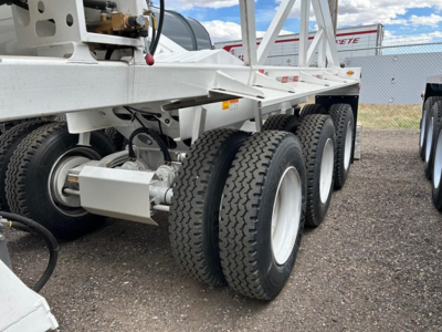 Trailer chassis with tandem axles and large dual tires, white frame, visible hydraulic hoses and equipment mountings on left side.