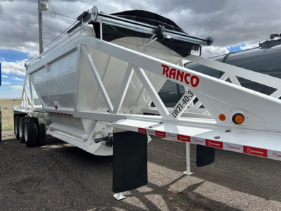 Trailer side of a RANCO Versa dump trailer showing white metal frame and diagonal braces, with red RANCO logo on side; wheel axles and black mud flaps visible.