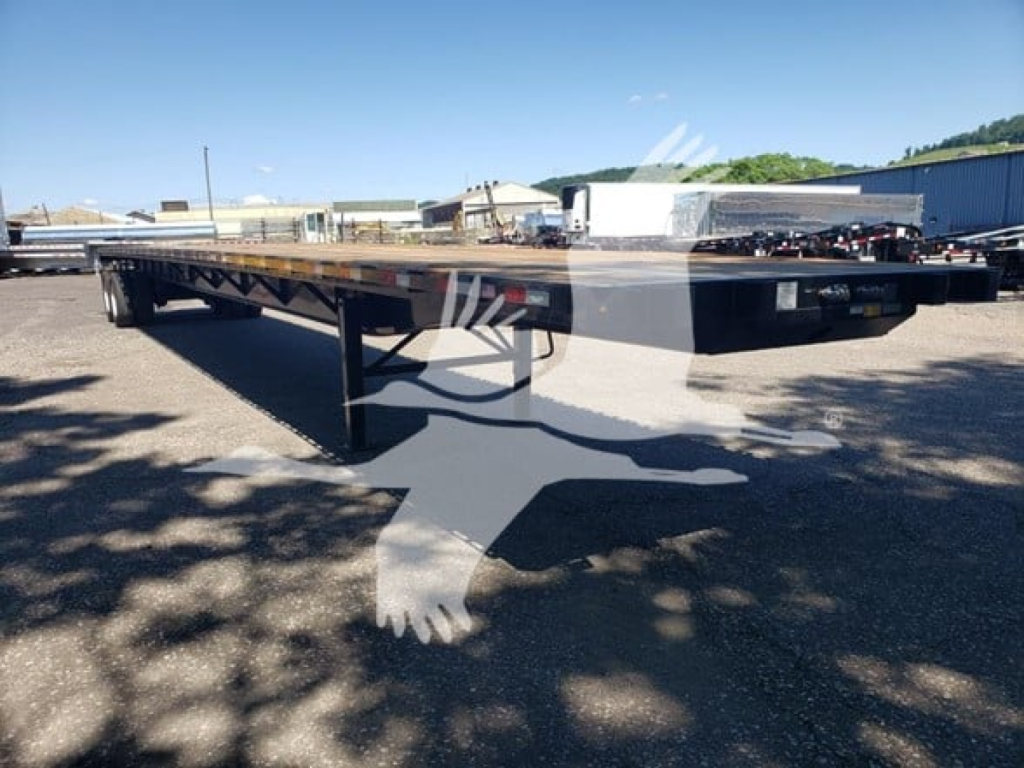 Flatbed trailer showing long steel deck and support legs, black frame, and undercarriage in an outdoor lot.
