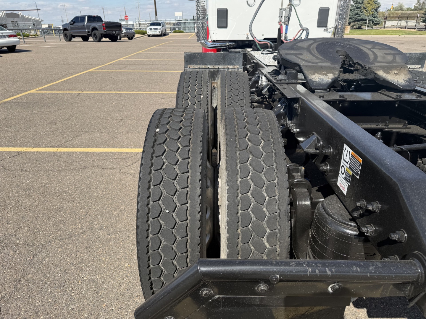 Dual rear wheels on a Kenworth truck chassis showing tires and suspension components with a white cab in background.