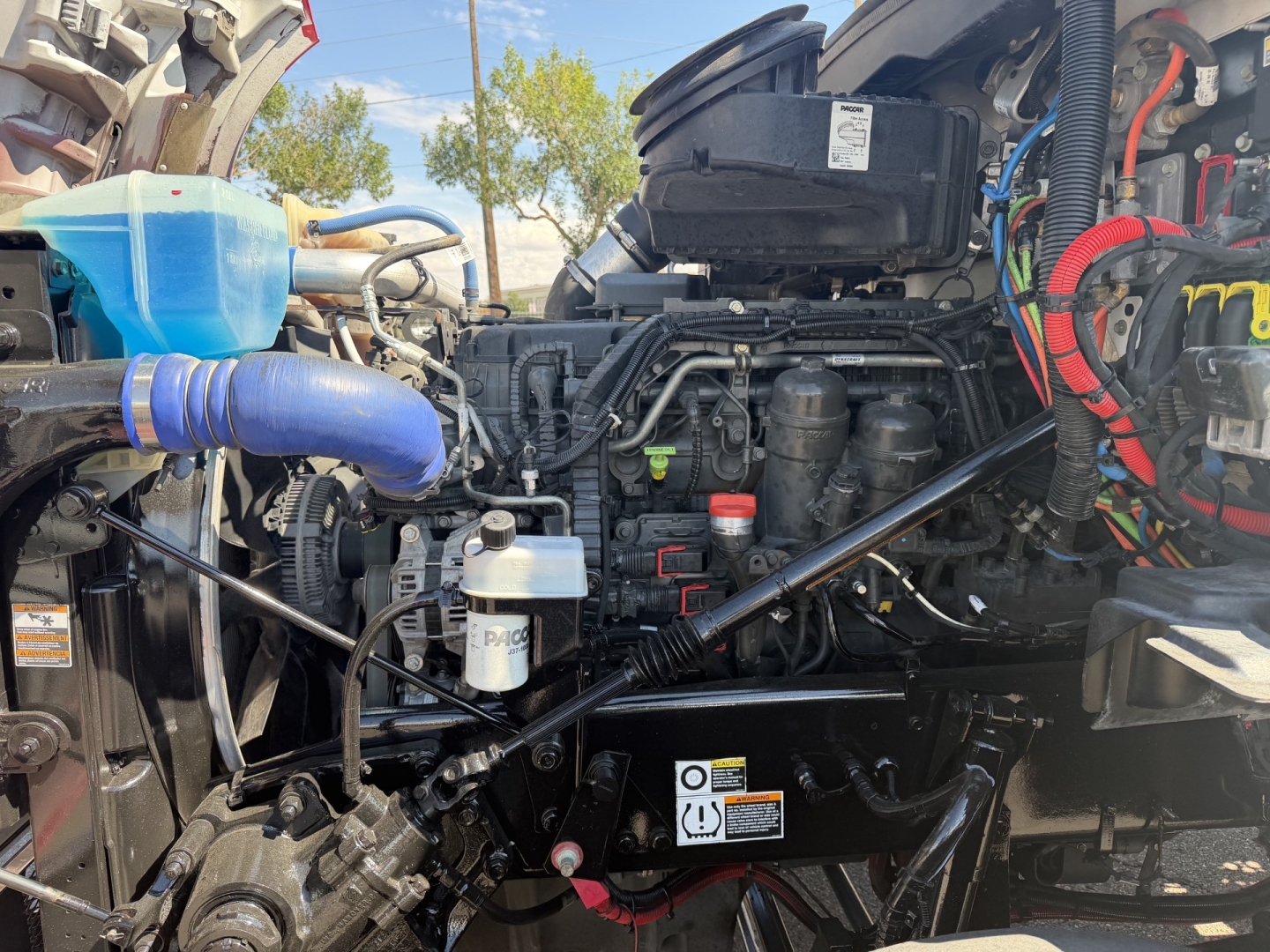 Kenworth T880 engine bay showing coolant reservoir, hoses, and engine components in a daycab truck.