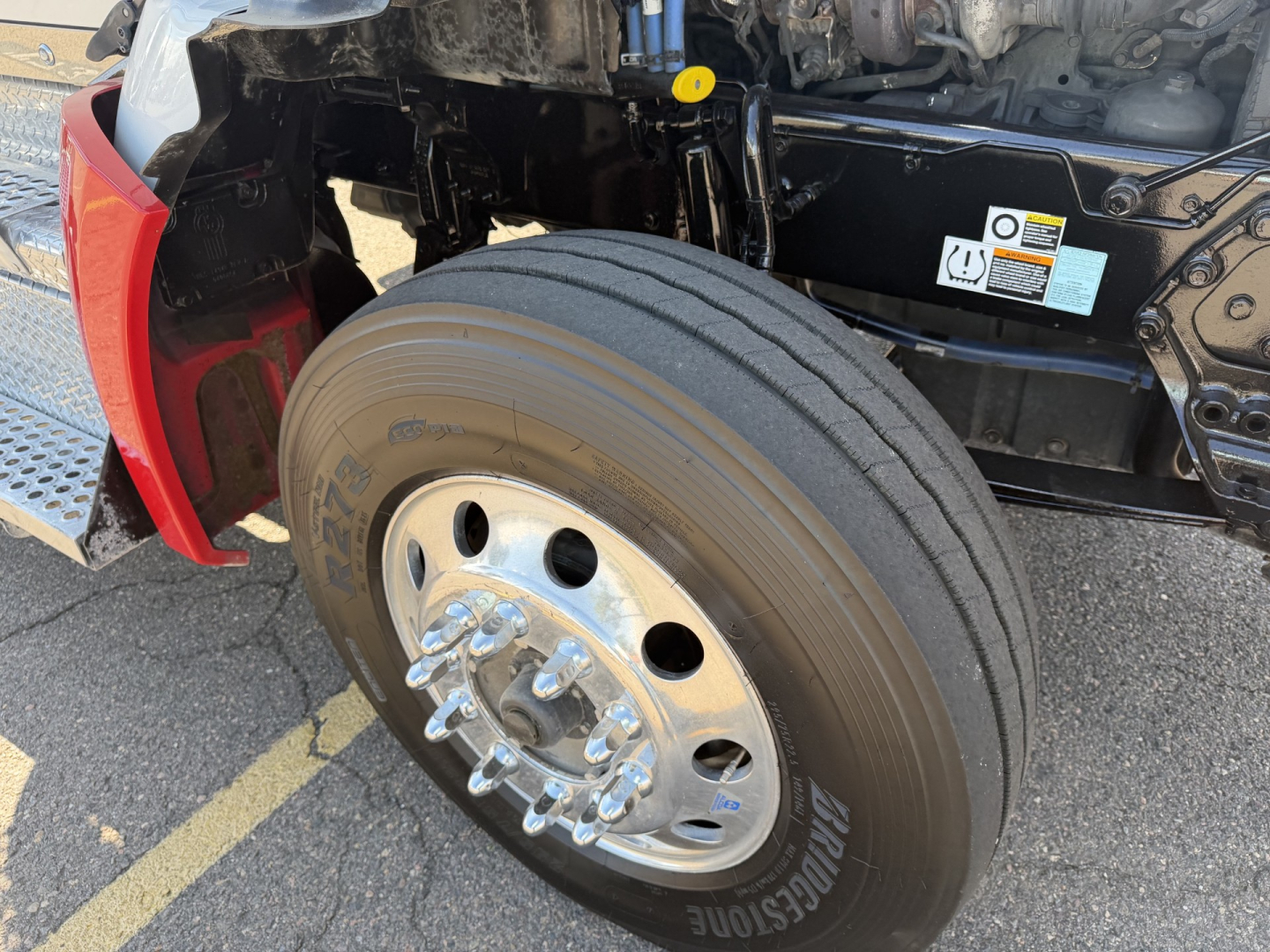 Kenworth T880 front wheel and suspension area showing front tire and chrome hub, with fender and under-hood components visible