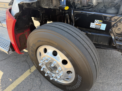 Kenworth T880 front wheel and suspension area showing front tire and chrome hub, with fender and under-hood components visible