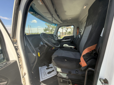 Truck cab interior showing driver seat and steering wheel in Kenworth T880 cab; visible dash controls, steering column, driver and passenger seats with seat belts; paper floor mat on the floor.