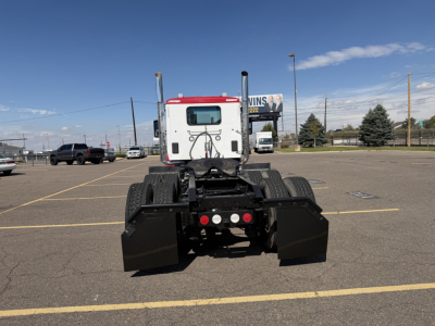 Kenworth T880 rear view showing fifth wheel and dual rear axles with black mud flaps and bumper, cab in white with red roof, clear sky.
