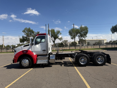 Kenworth T880 truck chassis in a parking lot with red and white cab, dual rear axles, side view showing fuel tanks and steps.