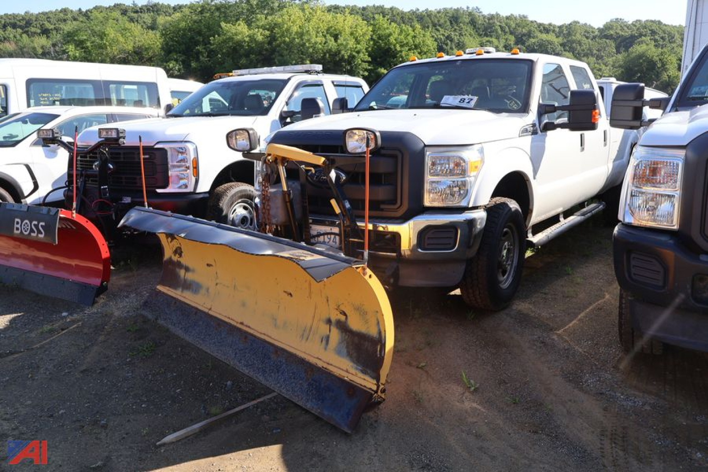 Ford F-350 Super Duty pickup in a lot with snow plow attachments in front; white crew cab truck, other trucks visible in background.