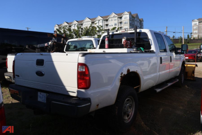 Ford F-350 Super Duty pickup truck rear-side view showing white crew cab with extended bed, toolbox rack, and various equipment in bed.