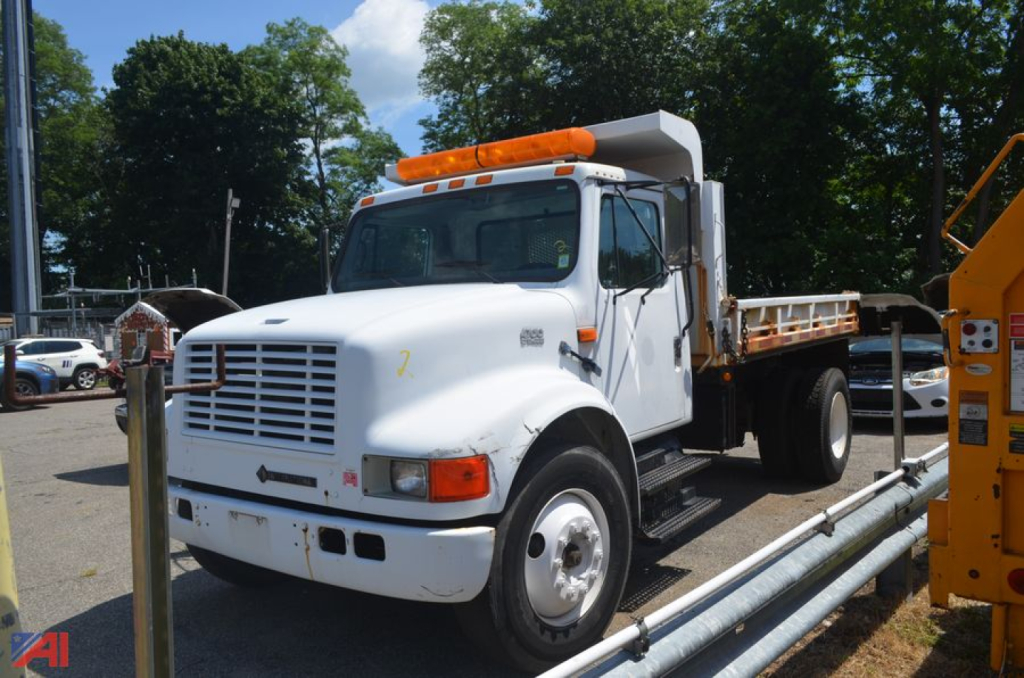 Dump truck 1996 International 4700 in/service showing white cab and dump bed with orange lights on top.
