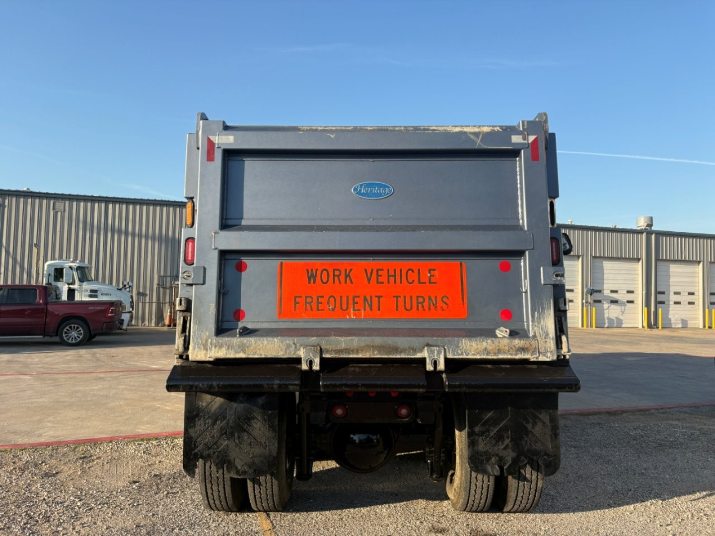 Dump truck rear showing orange 'WORK VEHICLE FREQUENT TURNS' sign and Volvo logo on tailgate.
