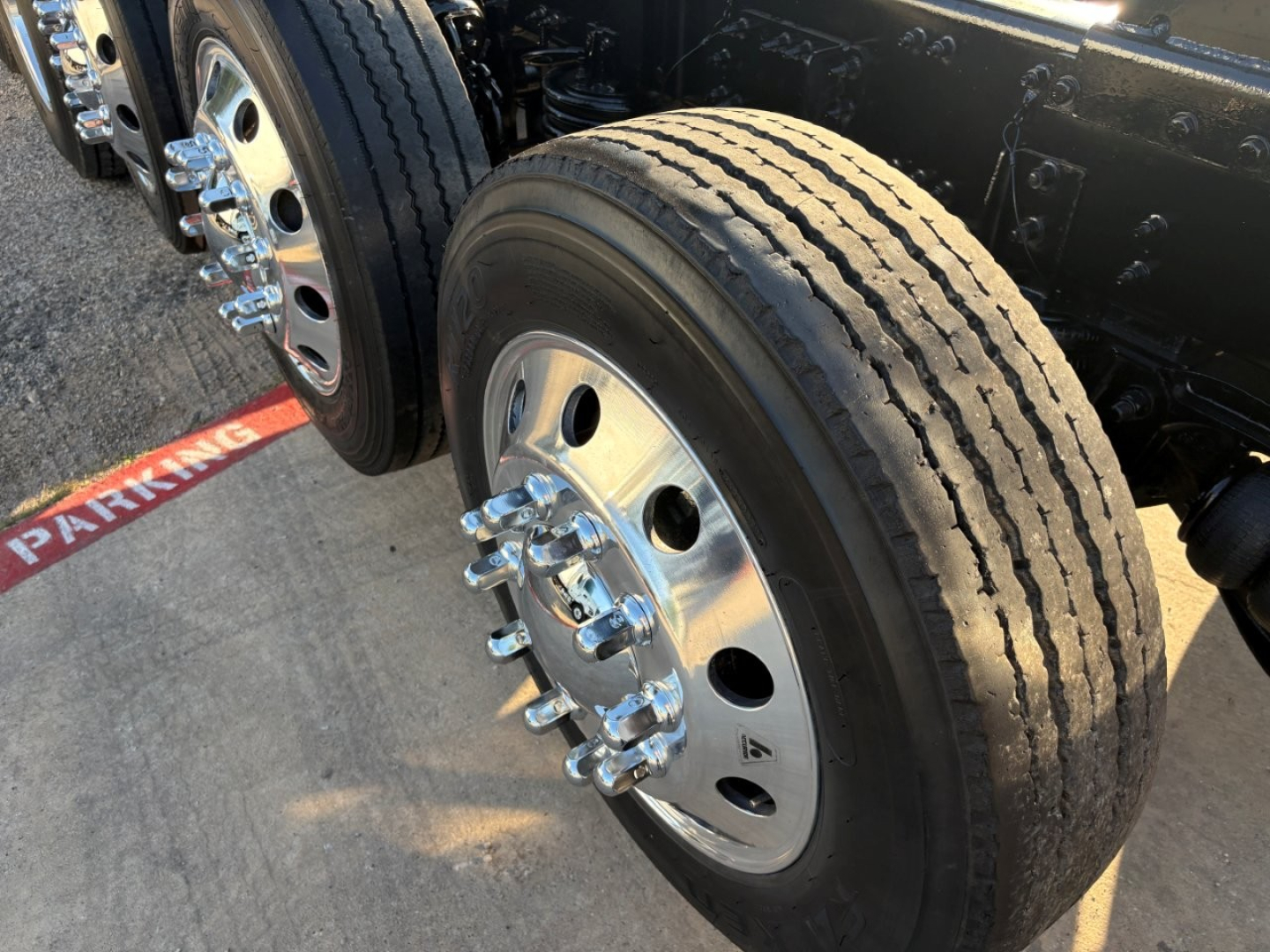 Truck front axle with a dual rear dual wheel setup, chrome lug nuts, and treaded tire visible on a Volvo dump truck chassis.