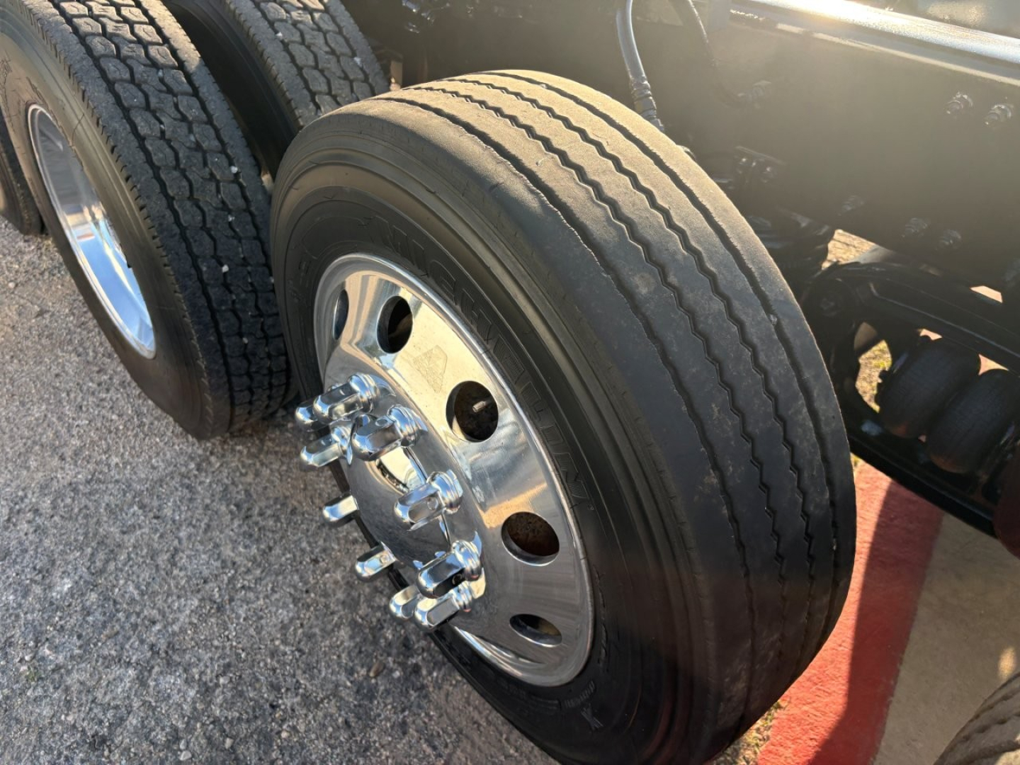 Truck wheel and dual rear axle visible with chrome lug nuts on aluminum hub; portion of chassis and tires visible.