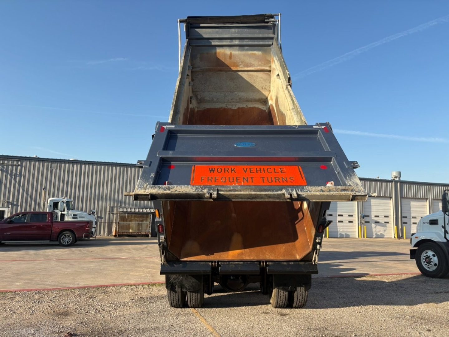 Dump truck rear view showing open dump bed raised, orange warning label, and Volvo branding on tailgate