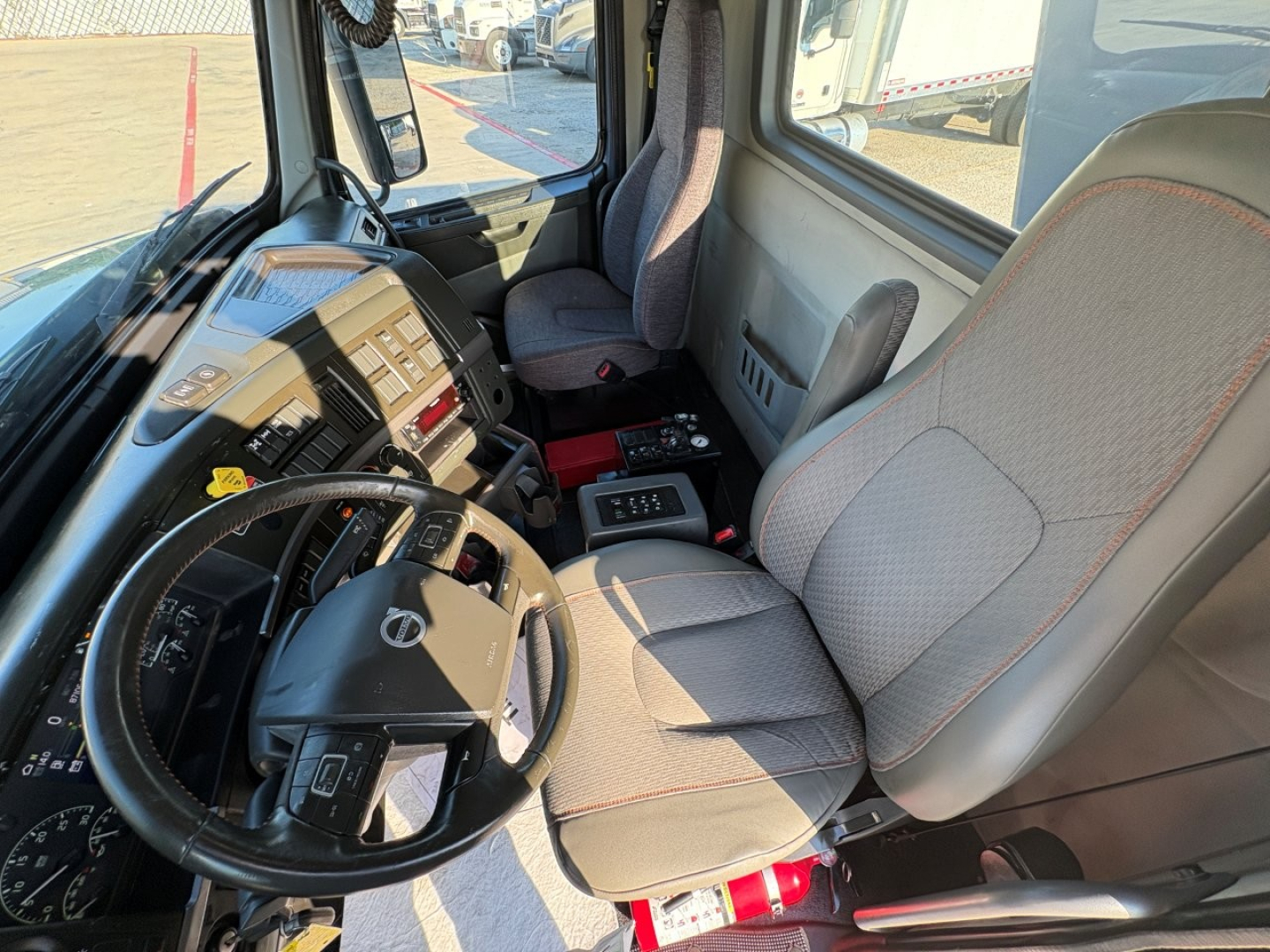 Interior of Volvo VHD104F300 cab showing steering wheel with Volvo emblem, dashboard with gauges, center console, and two fabric seats.