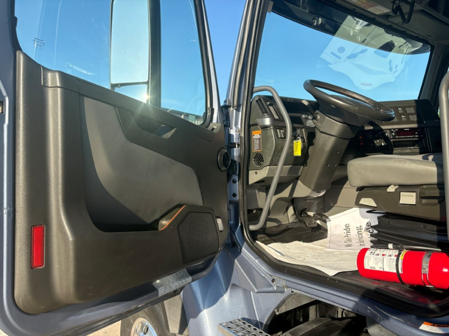 Volvo VHD104F300 dump truck interior cabin view from open driver door showing steering wheel dash pedals and floor mat