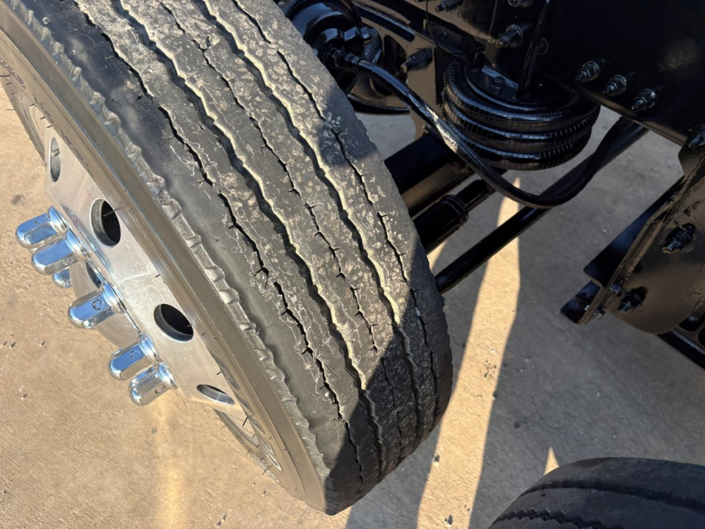 Truck front-left wheel and suspension components showing tire tread and hub with lug nuts.